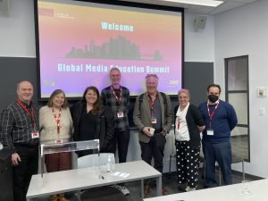 A photo of six people, 3 men, 3 women, in front of a screen that says "Welcome Global Media Education Summit"